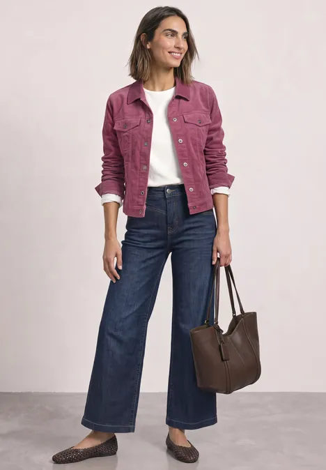 Frau in pinker Cordjacke über weißem Shirt, weiten Jeans, braunen Ballerinas und mit brauner Tasche.