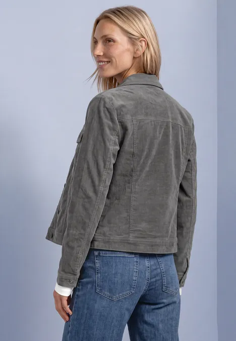 Femme en veste côtelée gris-vert et jean, regard par-dessus l'épaule