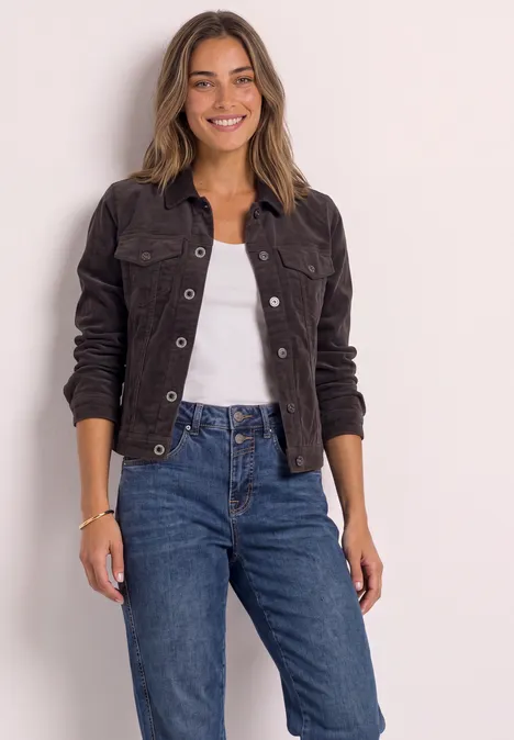 Femme souriante avec une veste noire, un top blanc et un jean bleu sur fond clair.