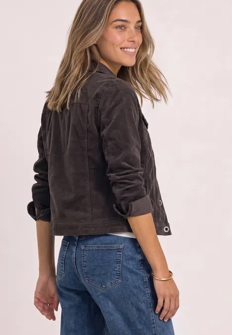 Femme souriante tourne la tête, porte veste brune courte et jean bleu