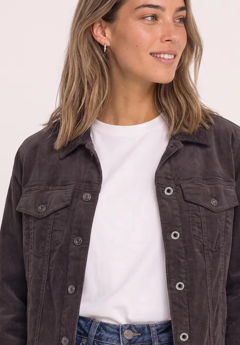 Une femme souriante en t-shirt blanc et veste en jean marron, vue de profil.