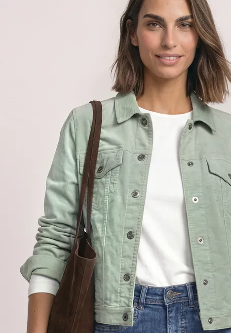 Jeune femme en veste en jean verte, T-shirt blanc et jean, avec un sac bandoulière marron.
