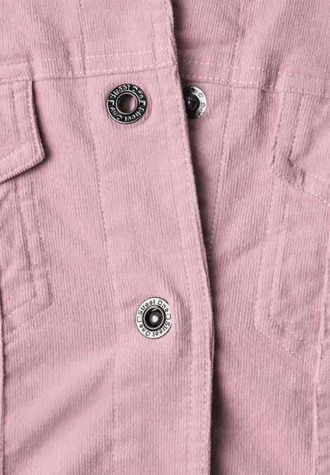 Gros plan d’une veste en velours côtelé rose avec boutons-pression métalliques.