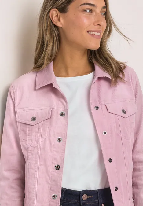 Femme souriante portant une veste en jean rose et un t-shirt blanc, regard de profil.