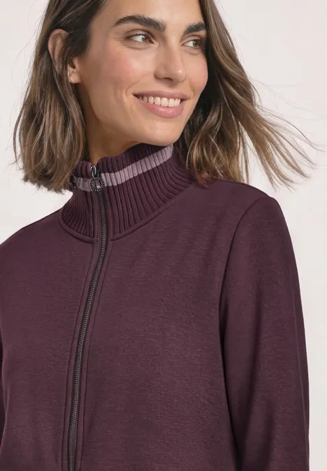 Veste de sport à col montant et détails en maille rustic rouge Frau mit schulterlangem Haar trägt einen violetten Pullover mit Reißverschluss und hohem Kragen.