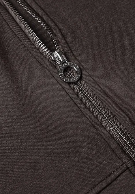 Close-up van een bruin kledingstuk met een zilverkleurige rits en ronde rits-trekker.