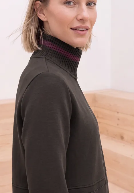 Blonde vrouw in donkere coltrui voor een lichte houten achtergrond.