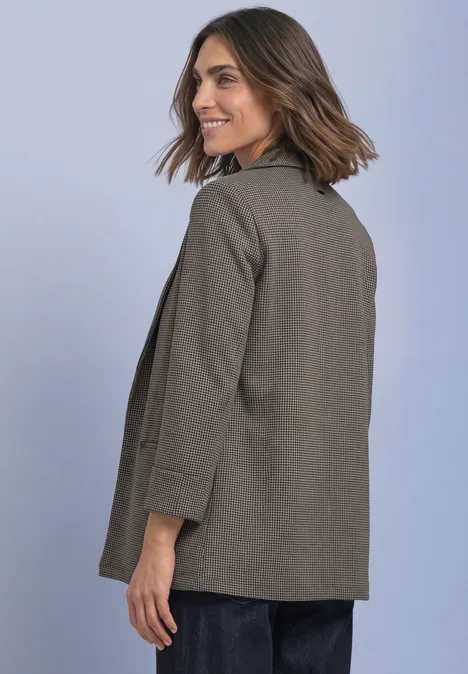 Eine Frau mit schulterlangem braunen Haar trägt einen olivgrünen Blazer und lächelt seitlich in die Kamera.