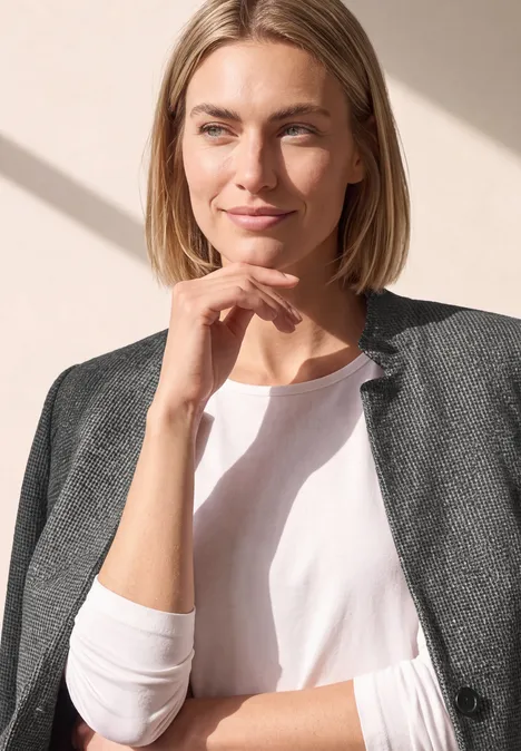 Porträt einer blondhaarigen Frau in weißem Shirt und grauem Blazer, die leicht lächelnd zur Seite blickt.