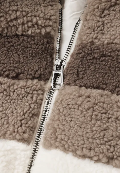 Nahaufnahme eines Reißverschlusses an einer braun-weißen Teddy-Fleecejacke.