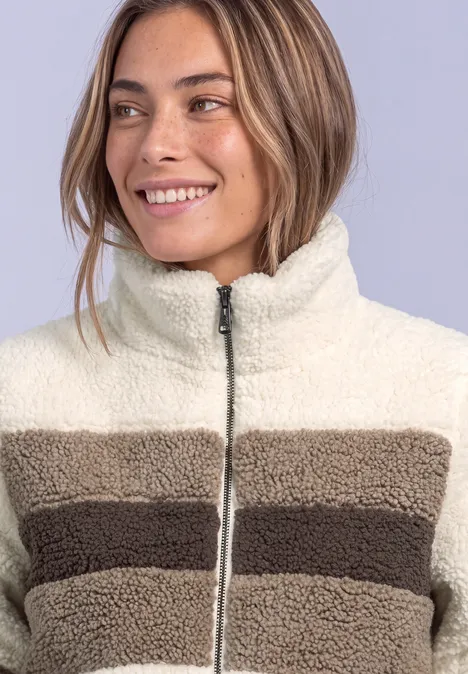 Frau lächelt und trägt eine gestreifte Fleecejacke in Cremeweiß und Braun.