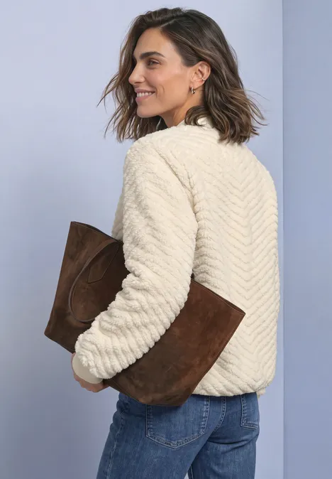 Vrouw draagt een crèmekleurige teddyjas en houdt een bruine suède clutch vast.
