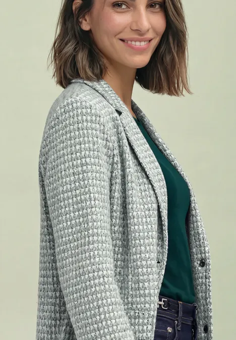 Eine lächelnde Frau in Blazer mit Hahnentrittmuster und dunkelgrünem Top vor hellem Hintergrund