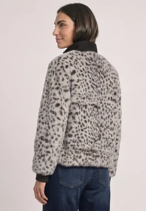 Frau in grauer Kunstfelljacke mit schwarzem Kragen und Leopardenmuster, seitlich stehend.