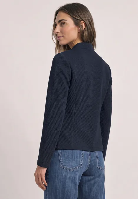 Een vrouw van achteren draagt een donkerblauwe blazer en blauwe jeans.