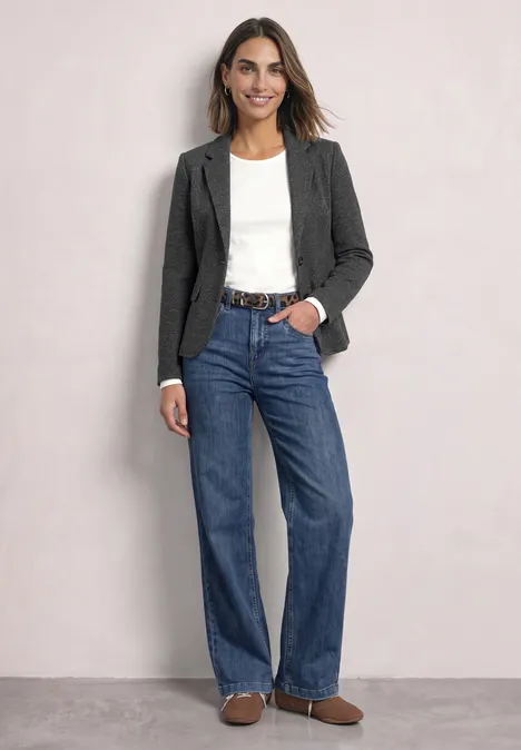 Eine Frau trägt Jeans, weiße Bluse, grauen Blazer und braune Schuhe.
