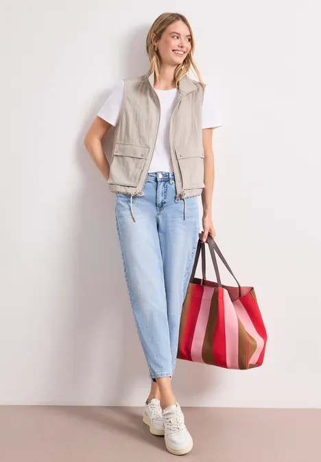 Frau mit Weste, T-Shirt, Jeans und großer roter Tasche.