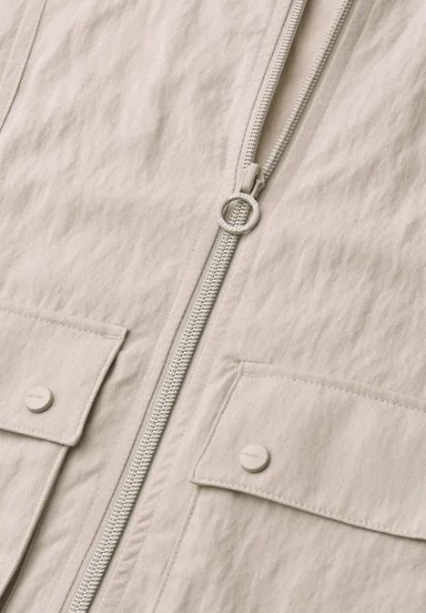 Beige Jacke mit durchgehendem Reißverschluss und zwei Klappentaschen mit Druckknöpfen.