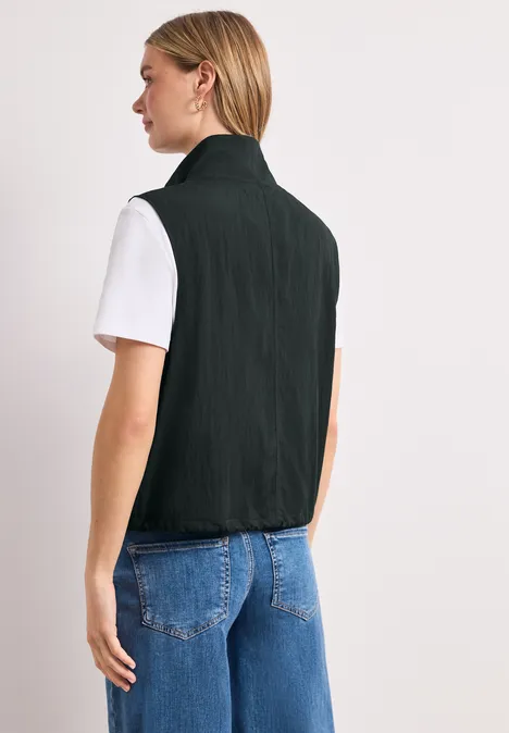 Achteraanzicht van een persoon met een zwart gilet, een wit T-shirt en een blauwe spijkerbroek.