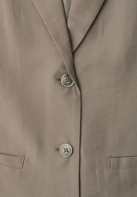 Close-up van een taupekleurig colbert met revers, twee knopen en klepzakken.