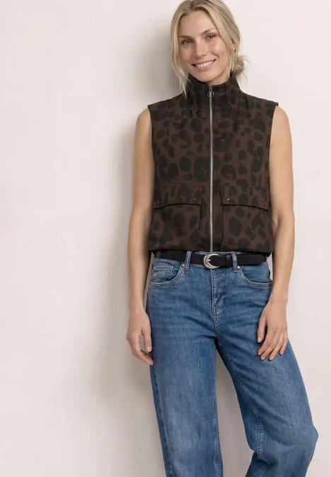 Modell in ärmelloser Leo-Weste mit Reißverschluss und blauen Jeans vor hellem Hintergrund.