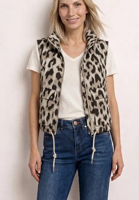 Eine Person trägt ein weißes T-Shirt, eine ärmellose Jacke mit Leopardenmuster und blaue Jeans.