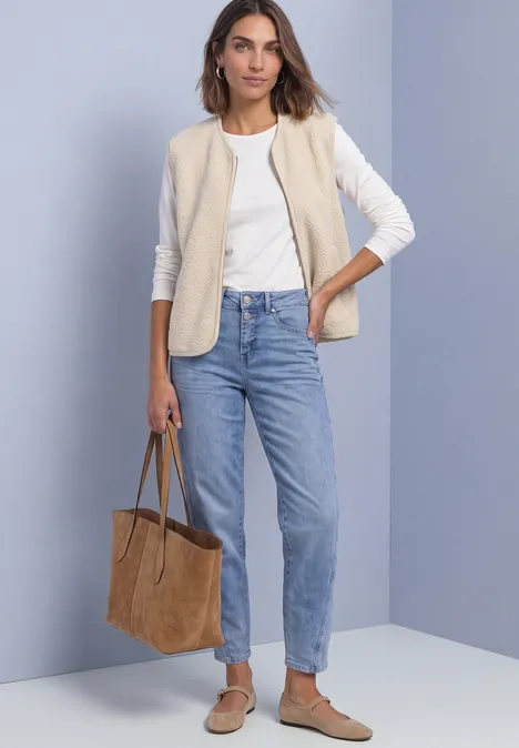 Frau trägt weiße Langarmbluse, beiges Steppweste, helle Jeans, braune Wildleder-Loafers und große Wildleder-Tasche.