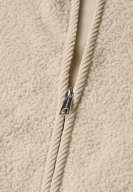 Nahaufnahme eines beigen Teddy-Fleece-Oberteils mit Reißverschluss und Kordelzug.