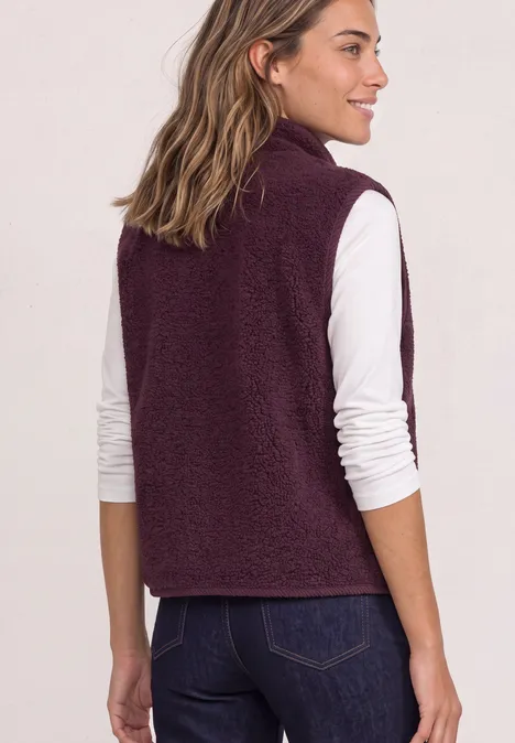 Vrouw van achteren met wit shirt met lange mouwen en bordeaux fleecebodywarmer, kijkt naar links.