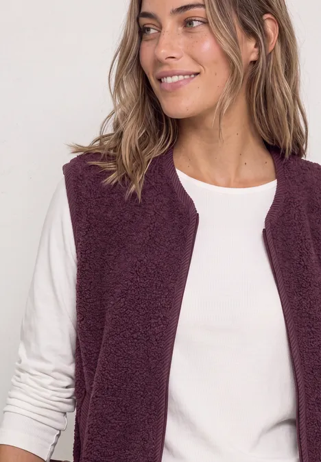 Een glimlachende vrouw in een wit shirt met lange mouwen en paarse fleecebodywarmer