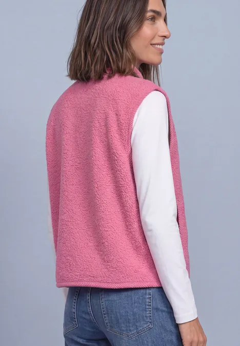 Vrouw van achteren in een roze teddyvest met een wit shirt met lange mouwen en een blauwe spijkerbroek.
