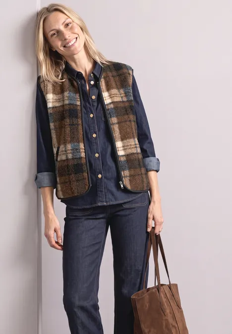 Gilet en peluche à fermeture zip et détails en velours côtelé Obsidian Blue Frau in Jeanshemd, Jeanshose und kariertem Weste, lächelnd, mit brauner Tasche.