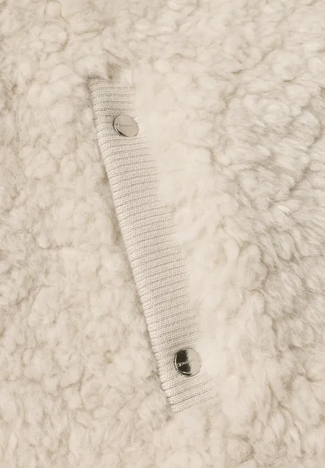Nahaufnahme eines cremefarbenen, flauschigen Fleece-Stoffs mit angenähtem Riemen und Metall-Snaps.
