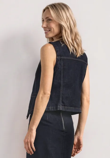 Achteraanzicht: persoon in mouwloze donkerblauwe denimvest en -rok met rits, neutrale achtergrond