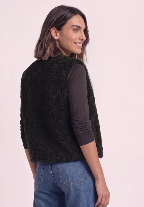 Vrouw in profiel draagt zwarte, pluizige bodywarmer over een longsleeve en jeans.