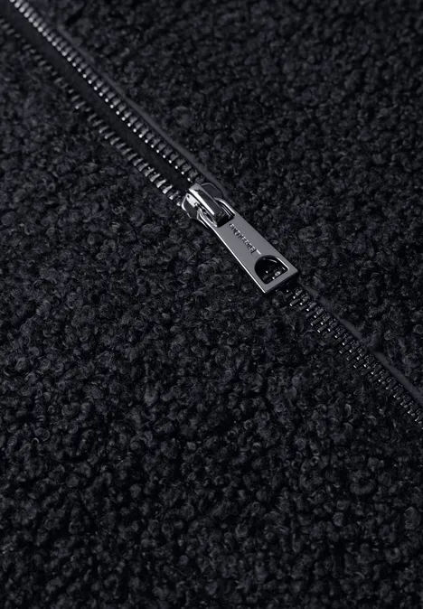 Close-up van een zwarte teddyfleece-stof met een zilverkleurige metalen rits.