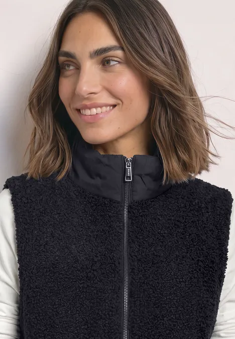 Vrouw met zwarte teddy-fleece bodywarmer met rits en opstaande kraag, glimlachend opzij.