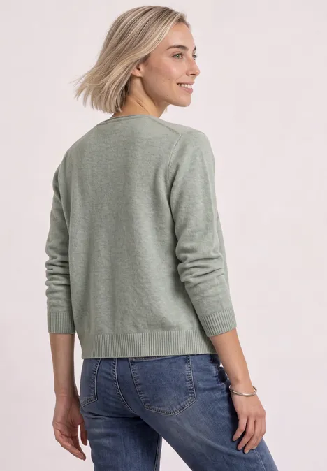 Cadigan mit V-Neck und Knopfleiste eucalyptus green mel. Frau von hinten in grünem Pullover und blonden Haaren trägt blaue Jeans vor hellem Hintergrund.