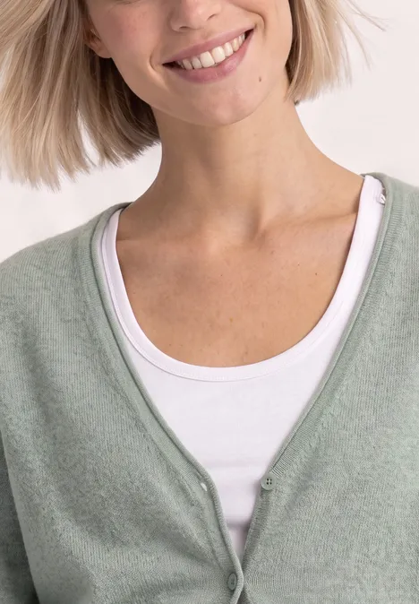 Cadigan mit V-Neck und Knopfleiste eucalyptus green mel. Frau trägt hellgrünen Cardigan über weißem Top, lächelt leicht.