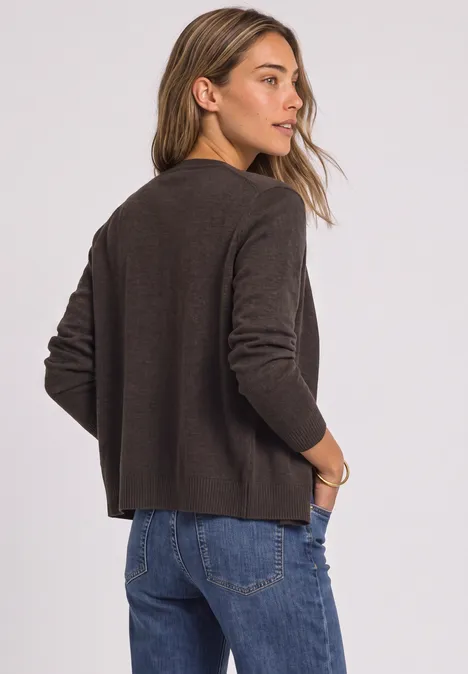Cadigan mit V-Neck und Knopfleiste black coffee mel. Frau steht seitlich, trägt braunen Pullover und Jeans, legt Hände in die Taschen und blickt über die Schulter.