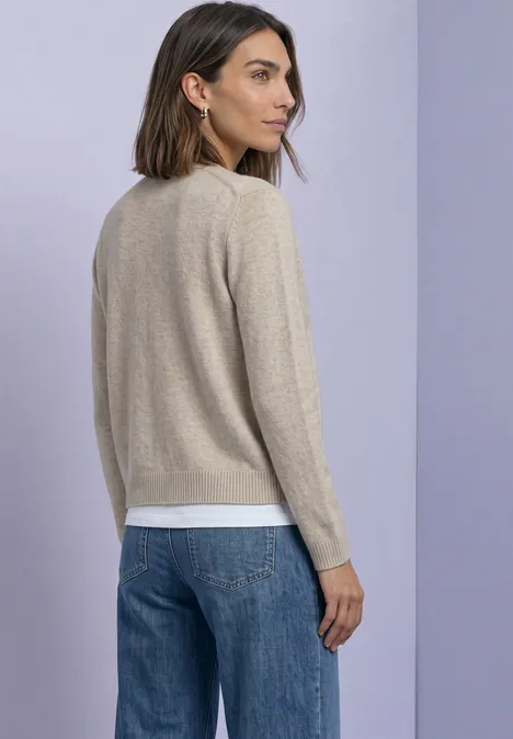 Cadigan mit V-Neck und Knopfleiste clay sand mel. Rückansicht einer Frau mit beigem Pullover, weißem Shirt und blauer Jeans vor lila Hintergrund.