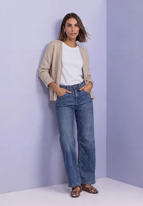 Cadigan mit V-Neck und Knopfleiste clay sand mel. Eine Frau mit weißem T-Shirt, beigem Cardigan, weiten Jeans und Leo-Sandalen vor violettem Hintergrund.
