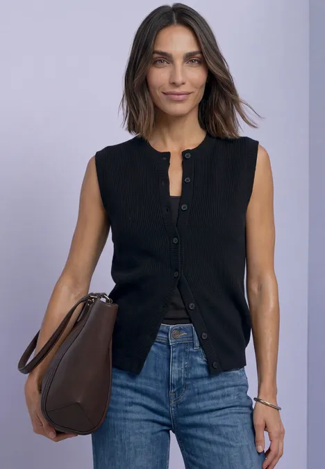 Strickweste mit Rundhals und Knopfleiste Black Eine lächelnde Frau in schwarzem, ärmellosem Cardigan, Jeans und großer brauner Tasche vor einfarbigem Hintergrund.