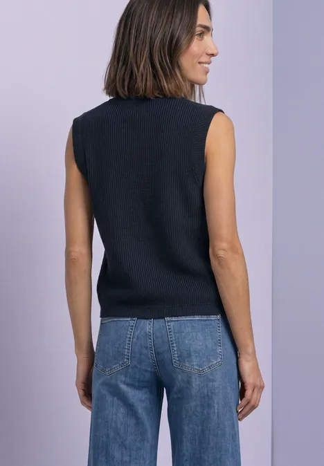 Eine Frau von hinten in ärmellosem schwarzem Top und Jeans vor hellem Hintergrund.