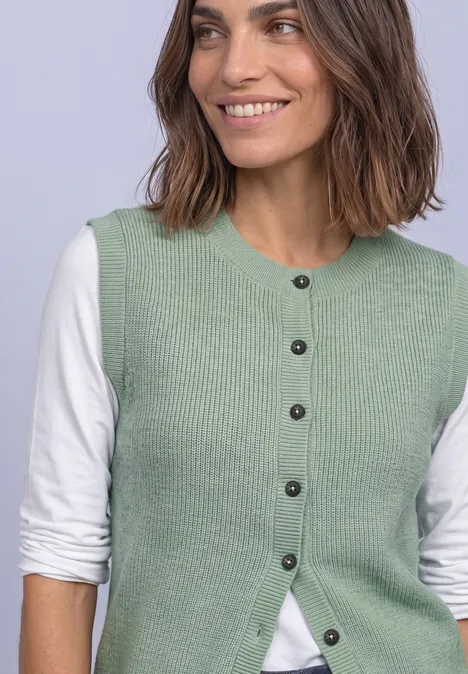 Lächelnde Frau in hellgrüner Strickweste und weißem Langarmshirt