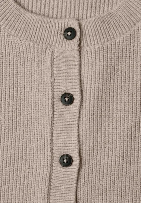 Beige Strickjacke mit Rippenbündchen und drei dunklen Kunststoffknöpfen mittig.