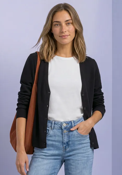 Frau in weißem T-Shirt, schwarzer Strickjacke und blauer Jeans, trägt eine braune Schultertasche