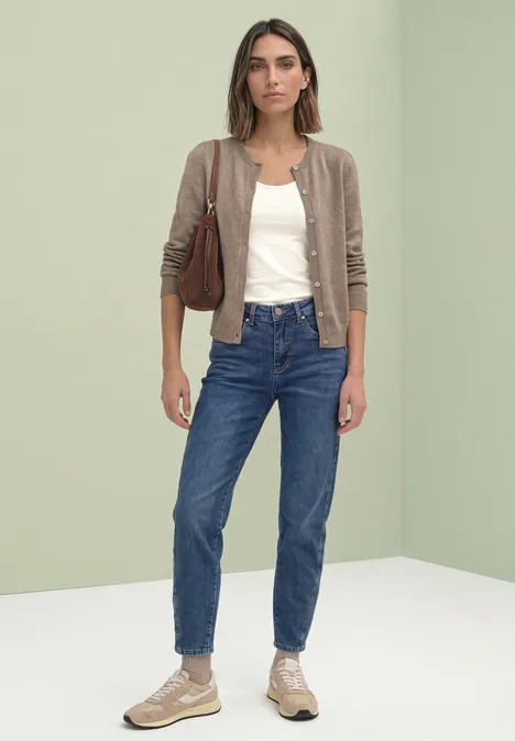 Frau in brauner Strickjacke, weißem Top, blauen Jeans, Sneakern und brauner Tasche