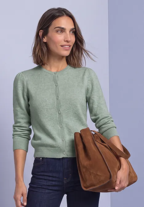Langarm Cardigan mit Rundhals und Knöpfen eucalyptus green mel. Eine Frau trägt eine grüne Strickjacke, dunkle Jeans und hält eine braune Tasche vor hellem Hintergrund.