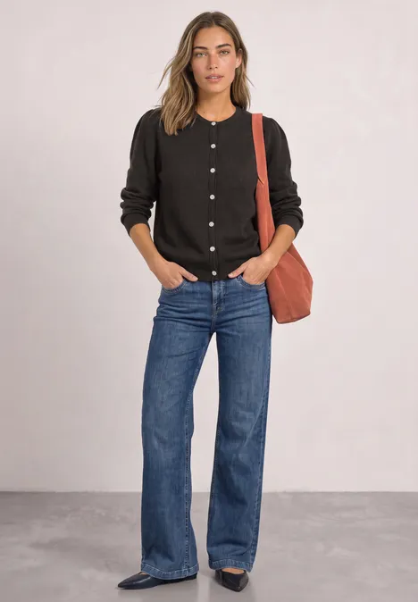 Langarm Cardigan mit Rundhals und Knöpfen black coffee mel. Eine junge Frau in schwarzer Strickjacke, blauen Jeans und roter Schultertasche, Hände locker in den Taschen.